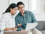 A couple sits on a couch reading a sheet of paper